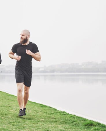 Couple jogging and running outdoors in park near the water. Young bearded man and woman exercising together in morning