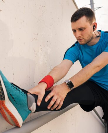 Young man runner getting ready to run stretching legs warm up quad stretch exercise on outdoor staircase